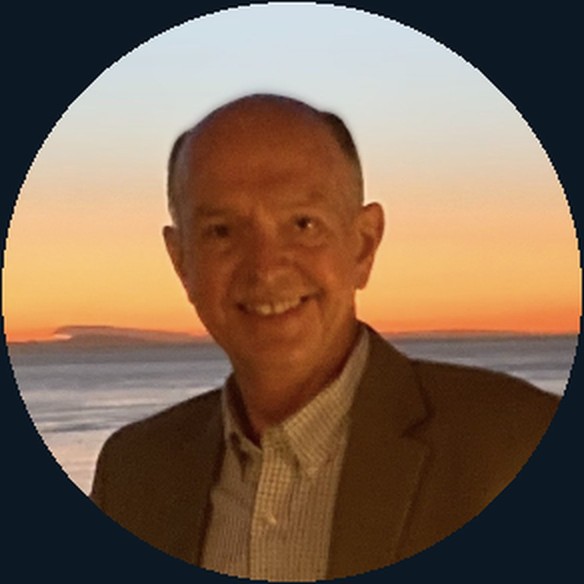 Greg D. Smith, founder of Experienced Radiology Consulting, in a tan jacket against a sunset shoreline.